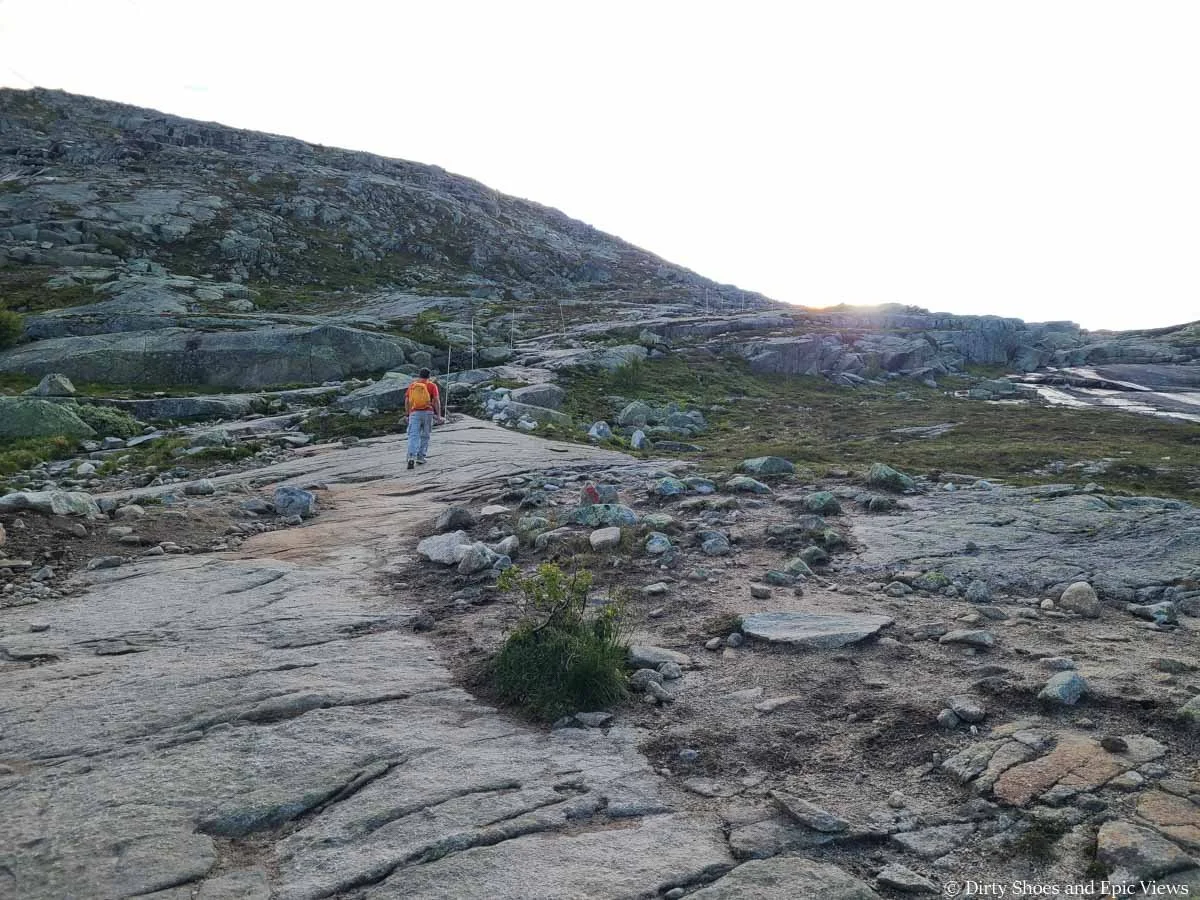 A hiker ascends a granite slab up a rocky pass on the Trolltunga hike