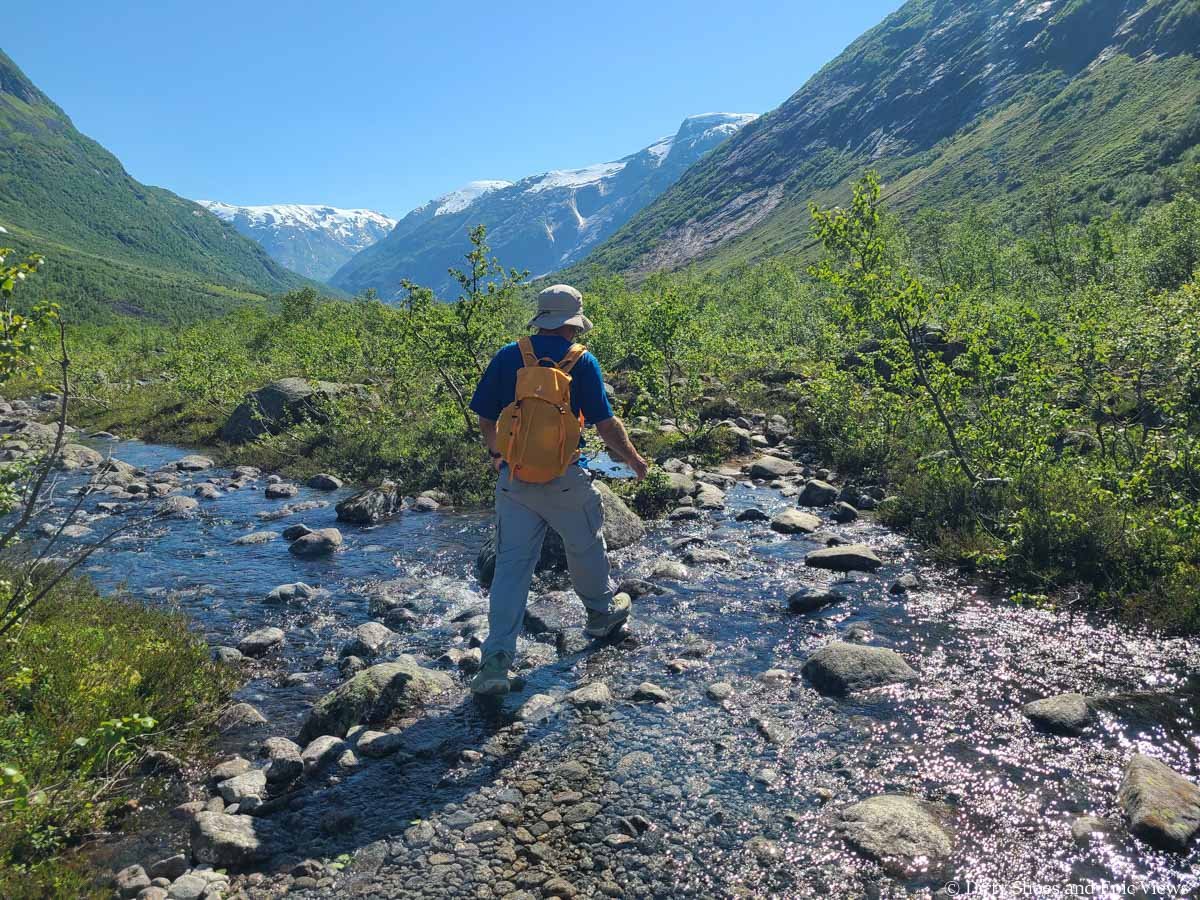 A hiker rock hops across a stream on the Austerdalsbreen hike in Norway