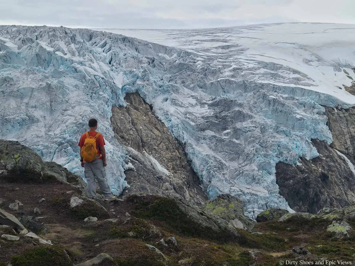 A hiker stands in front of a view of a massive icecap on the Reinanuten hike in Norway