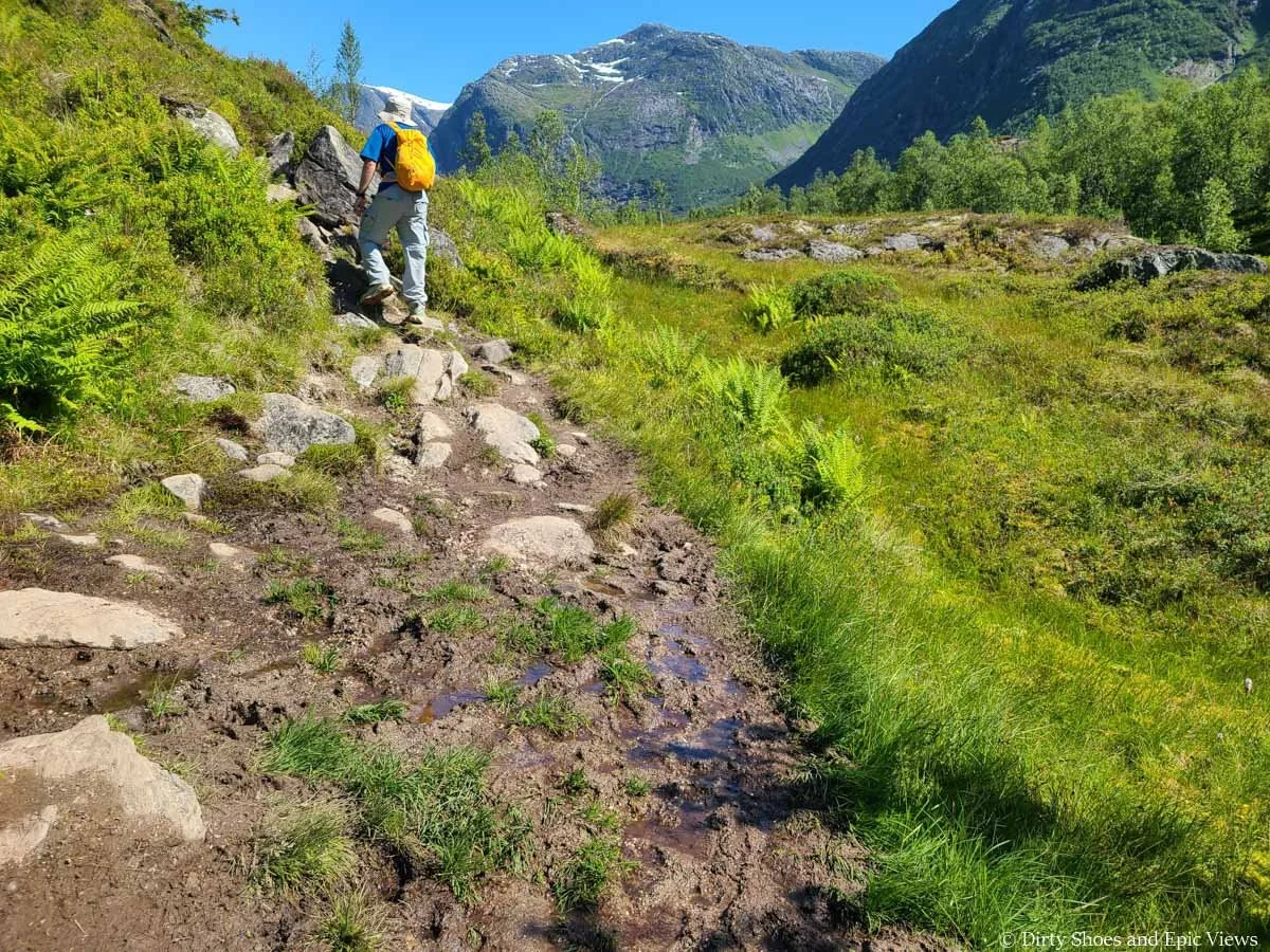 A hiker navigates a muddy and rocky patch of trail on the Austerdalsbreen hike