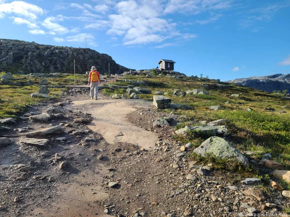 A hiker ascends a granite path towards a small shelter along the Trolltunga hike