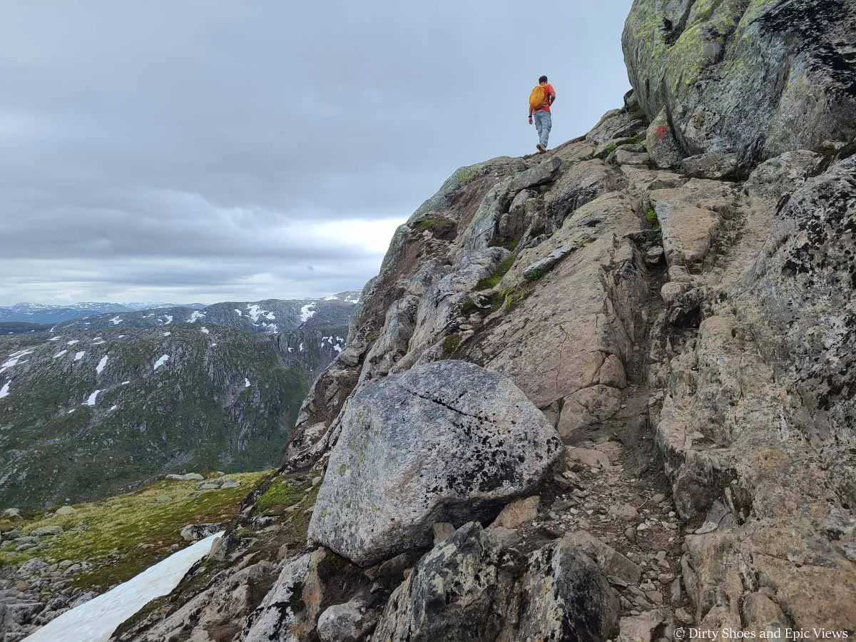 A hiker heads up a narrow rock ledge along the Reinanuten trail in Norway