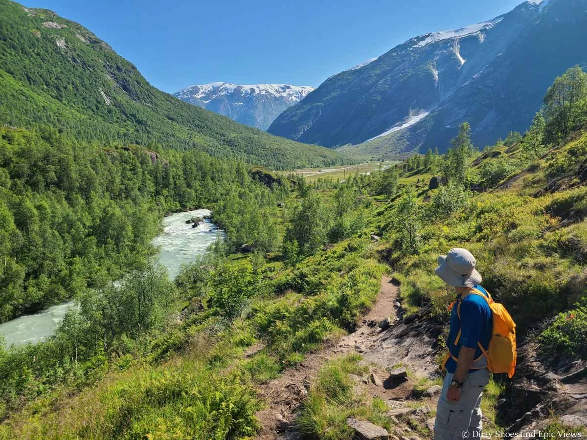 A hiker looks out over views of a blue stream and mountains from the Austerdalsbreen hike in Norway