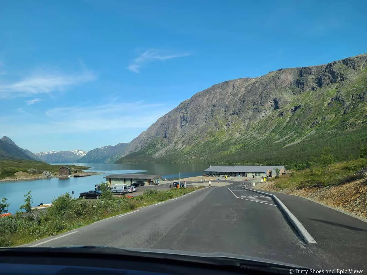 A road ends by a building and parking lot at the edge of a lake