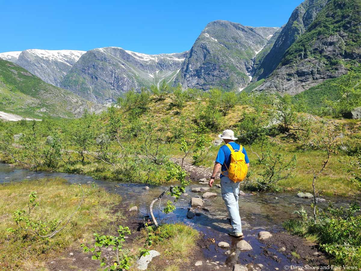 A hiker rock hops across a small stream towards mountain views on the Austerdalsbreen hike in Norway