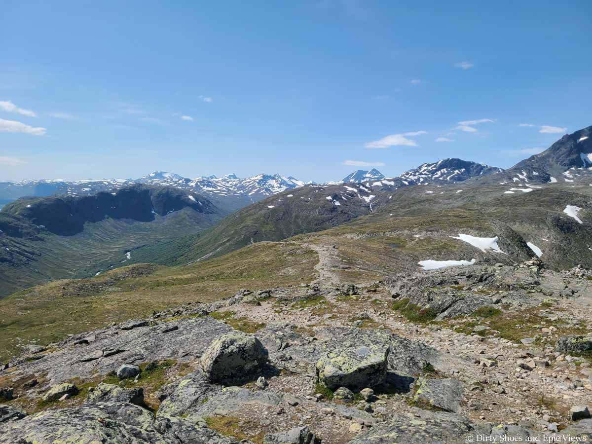 A narrow dirt path descends gently down a grassy slope towards mountain views on the Besseggen Ridge hike