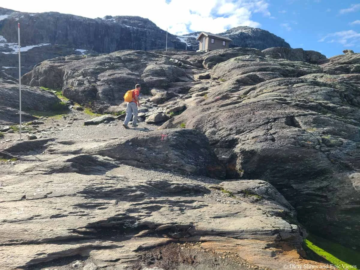 A hiker navigates a rocky climb up to a small shelter along the Trolltunga trail