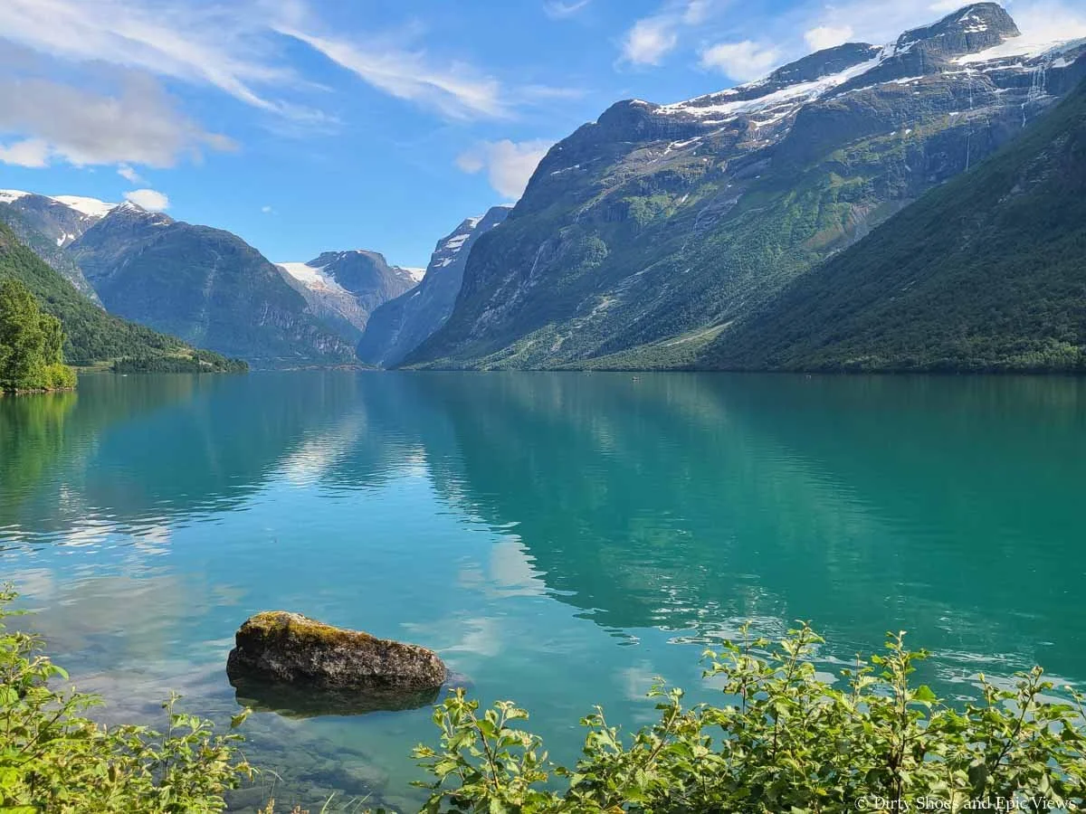 A bright blue lake sits beneath snow capped mountain at Lovatnet in Norway