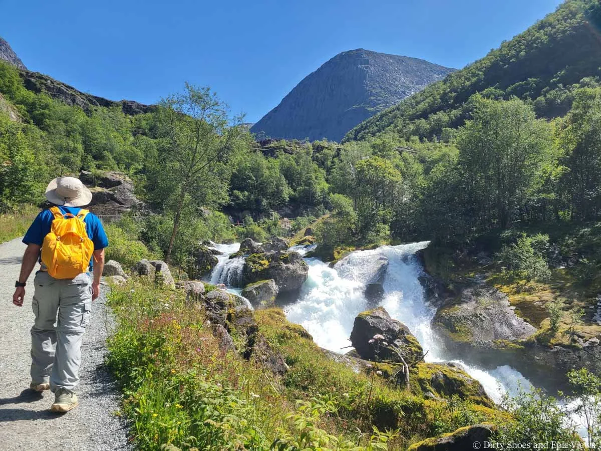 A hiker walks along a small powerful waterfall on the Briksdal Glacier hike