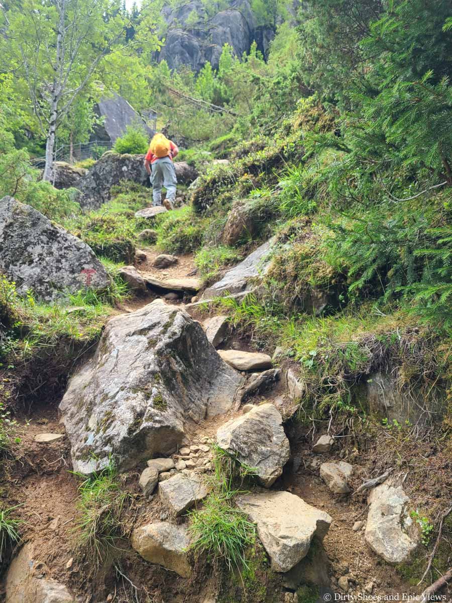 A hiker ascends a steep rocky path along the Reinanuten trail in Norway