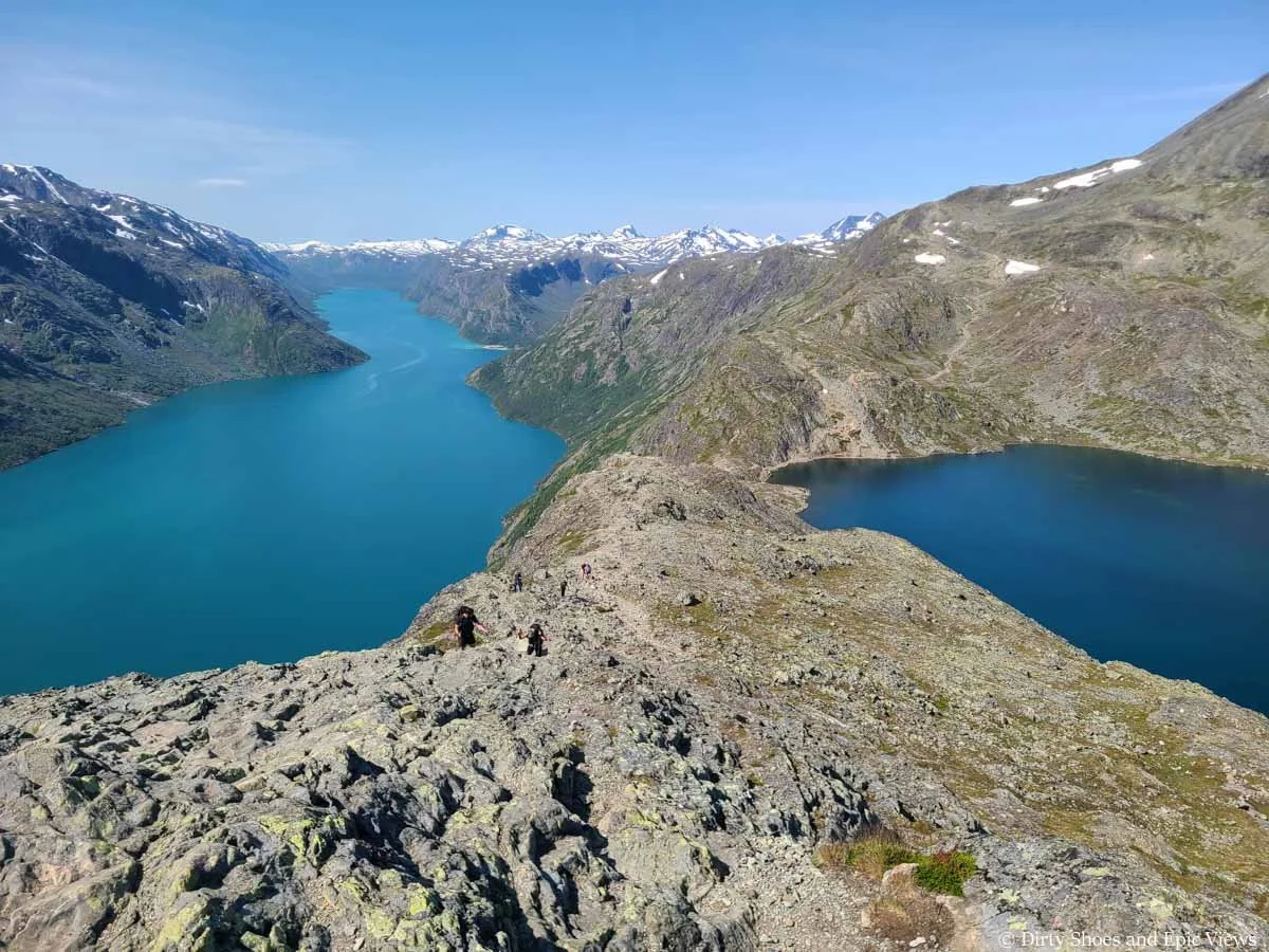 Looking down on hikers ascending a rocky ridge above two blue lakes on the Besseggen Ridge trail in Norway