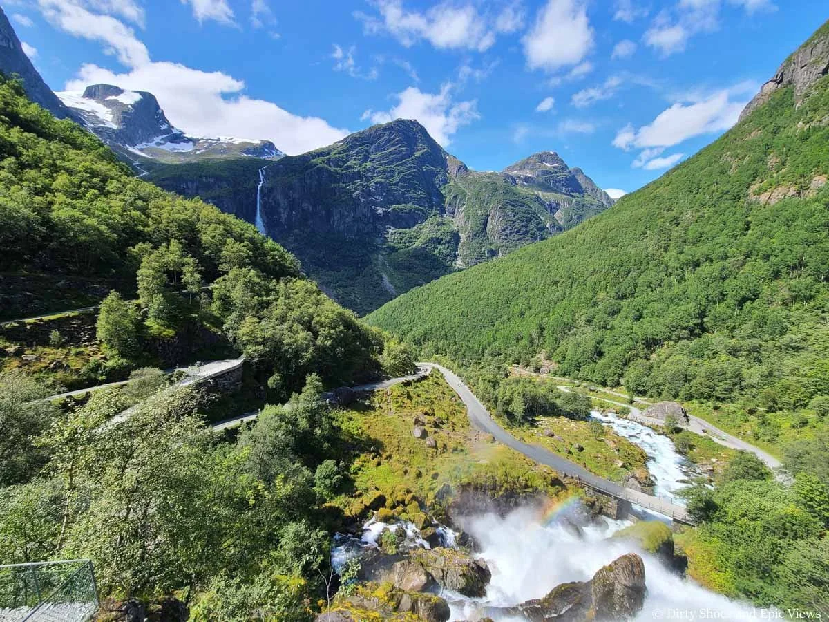 A paved walking path zigzags through the landscape with mountain views in the background on the Briksdal Glacier trail in Norway