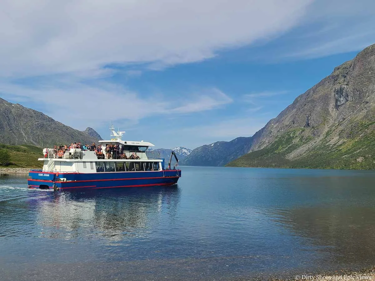 A small ferry carries people across a blue lake with mountain views for the Besseggen Ridge hike