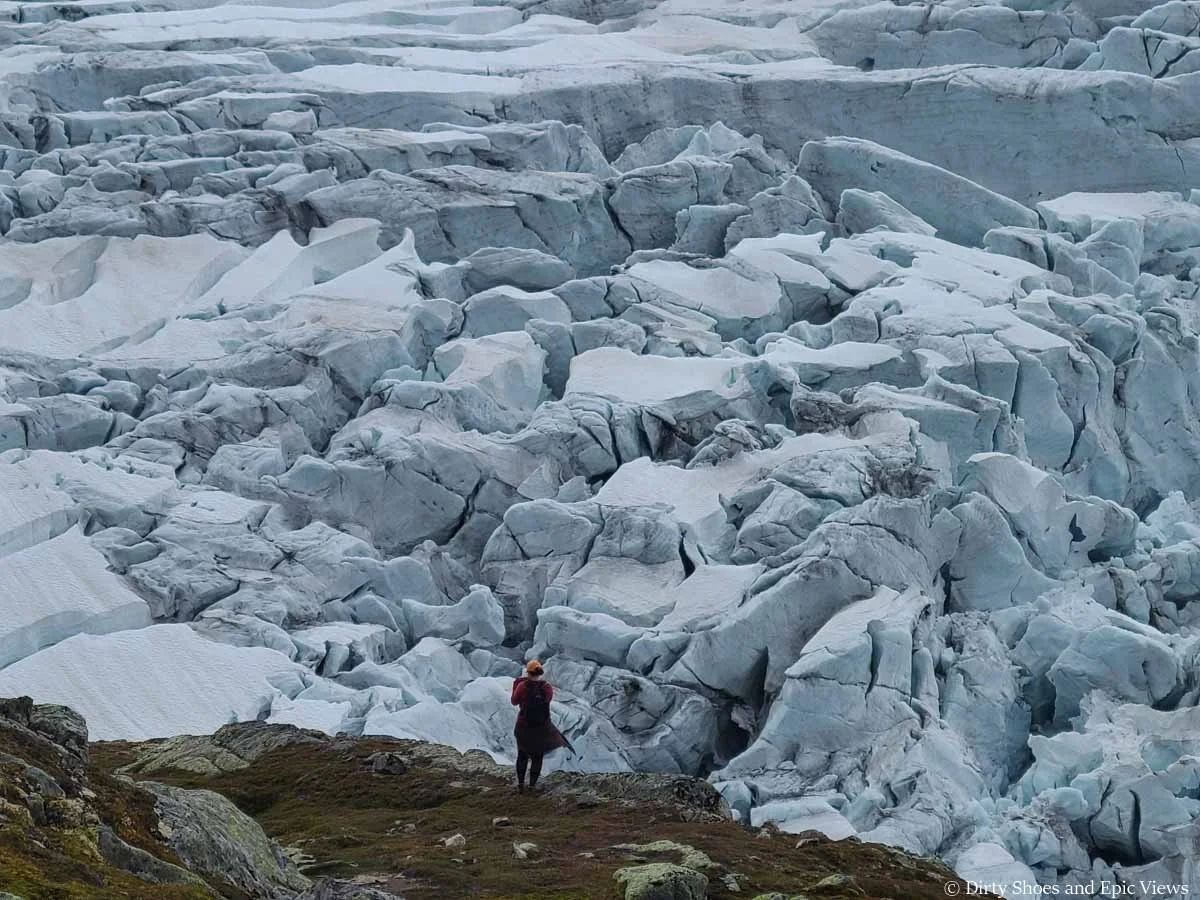 A hiker stands in front of a massive glacier at the Reinanuten viewpoint in Norway