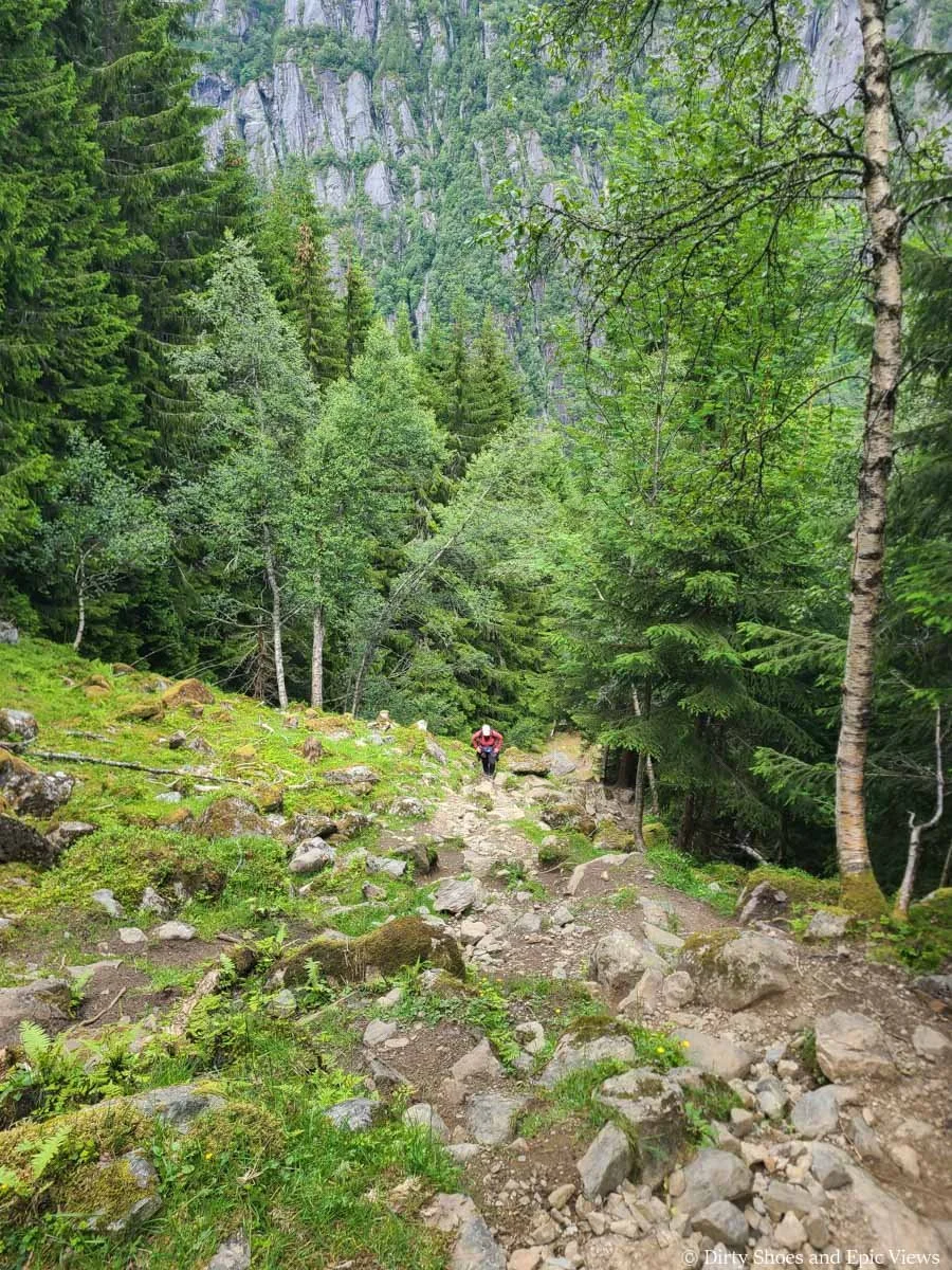 A view looking down a steep rocky path as a hiker ascends it as seen on the Reinanuten trail in Norway