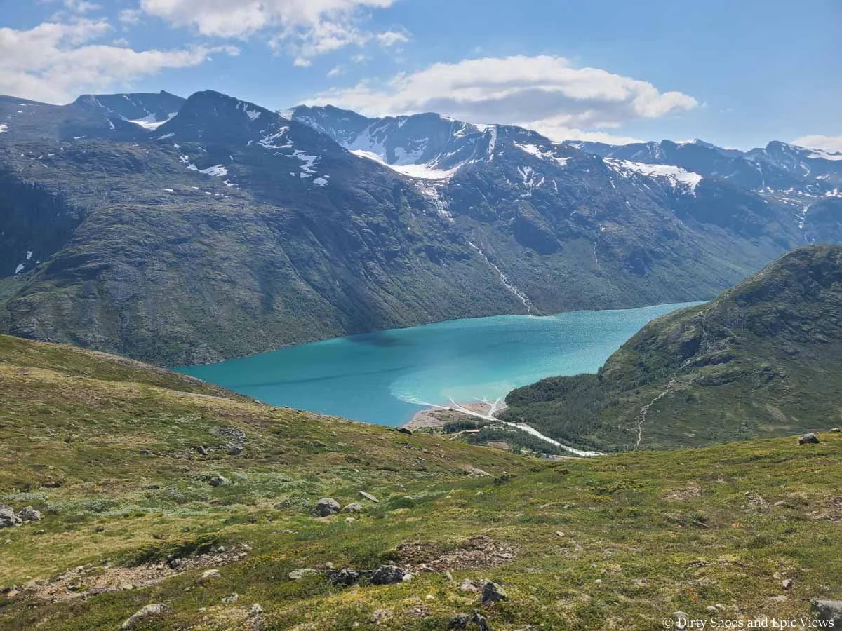Snowy mountains rise above a turquoise lake as seen from the Besseggen Ridge Trail in Norway