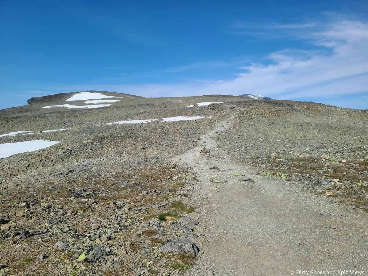 A clear herd path crosses a rocky landscape with snow patches on the Besseggen Ridge trail in Norway