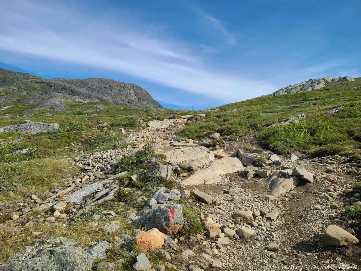 A path of loose rock gently ascends a grassy slope on the Besseggen Ridge trail in Norway