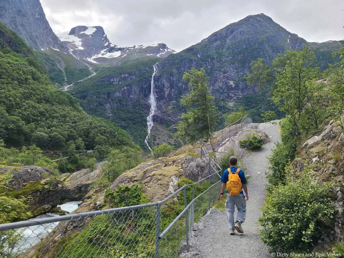 A hiker walks along a fenced pathway towards mountain views on the Briksdal Glacier trail in Norway