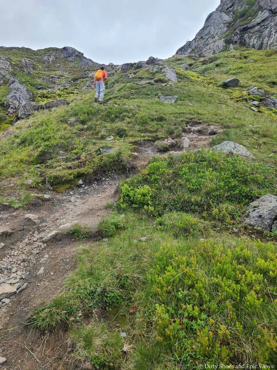 A hiker climbs a steep path towards the top of a headwall on the Reinanuten trail in Norway