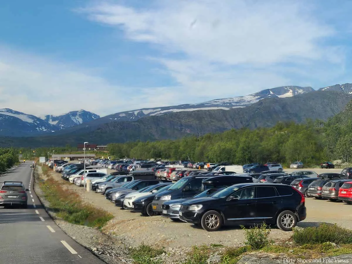 A large parking lot filled with cars sits in front of mountain views