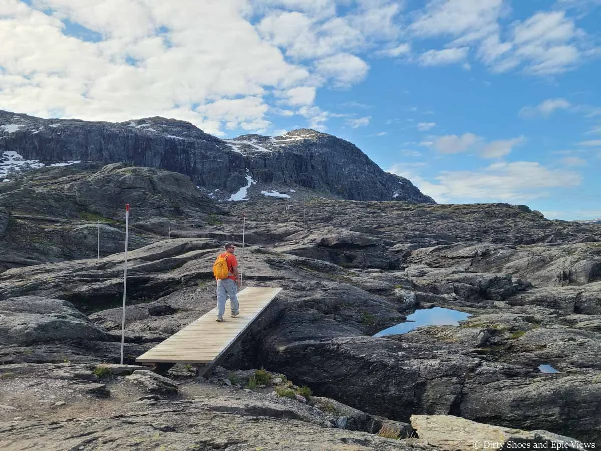 A hiker crosses a small wooden footbridge in a rocky landscape along the Trolltunga hike