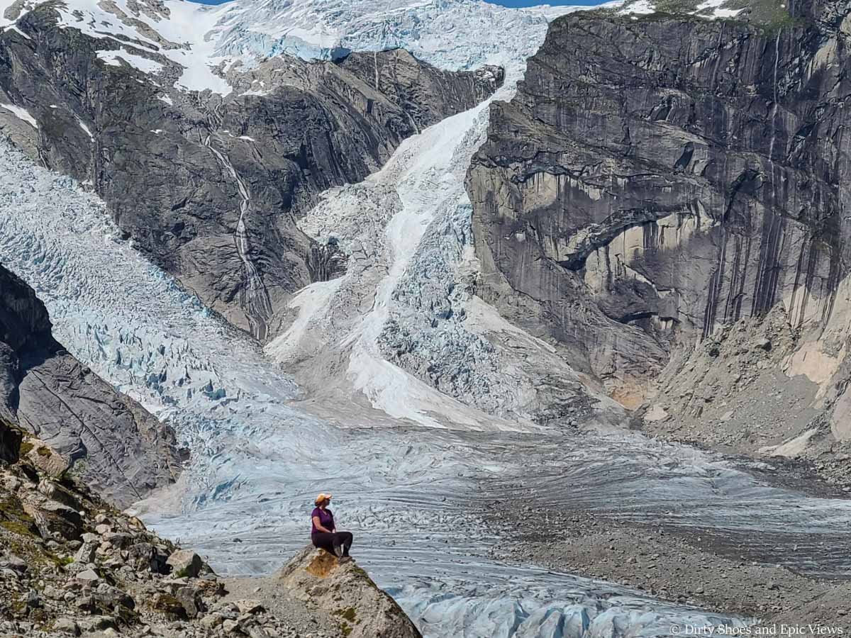 A hiker sits on a rock overlooking a massive cascading glacier on the Austerdalsbreen trail in Norway
