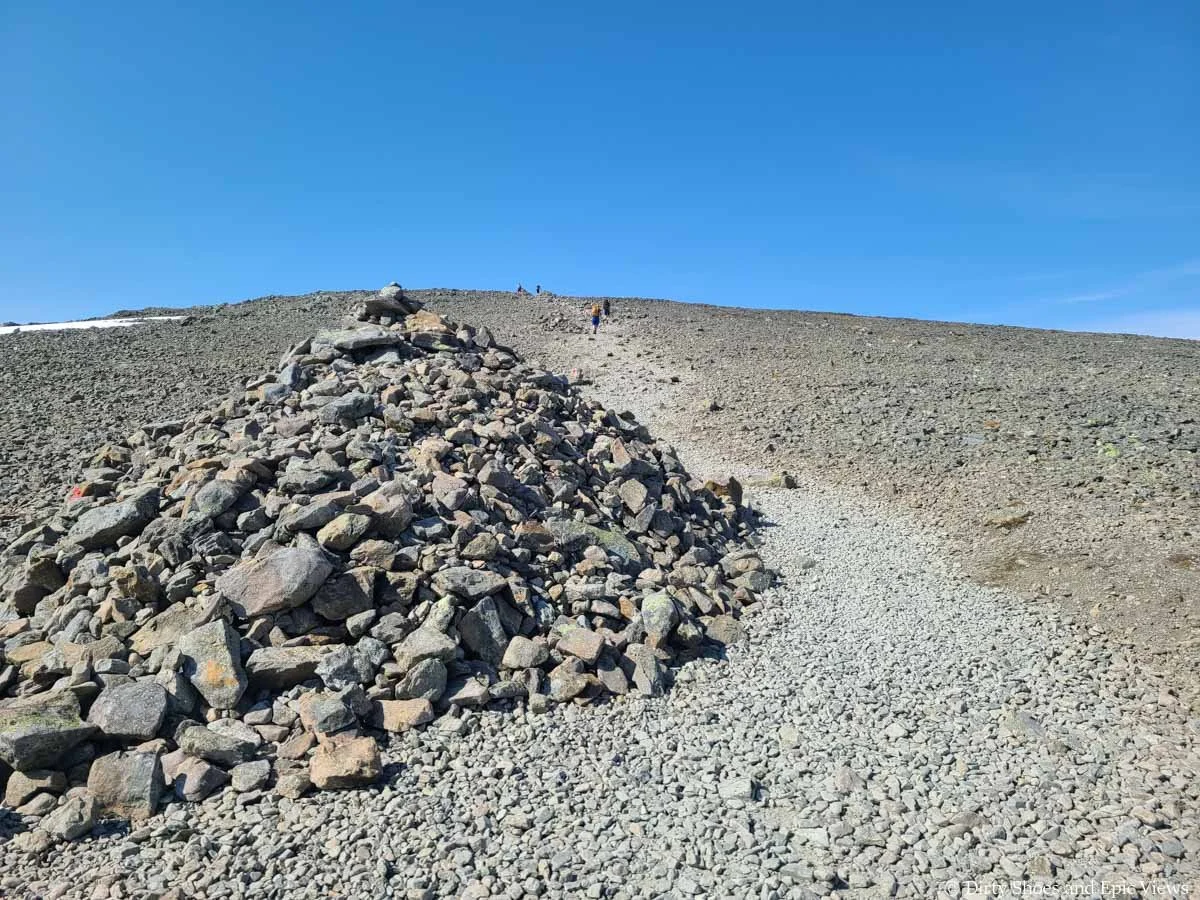 A large rock cairn sits along a herd path through a rocky landscape on the Besseggen Ridge trail in Norway