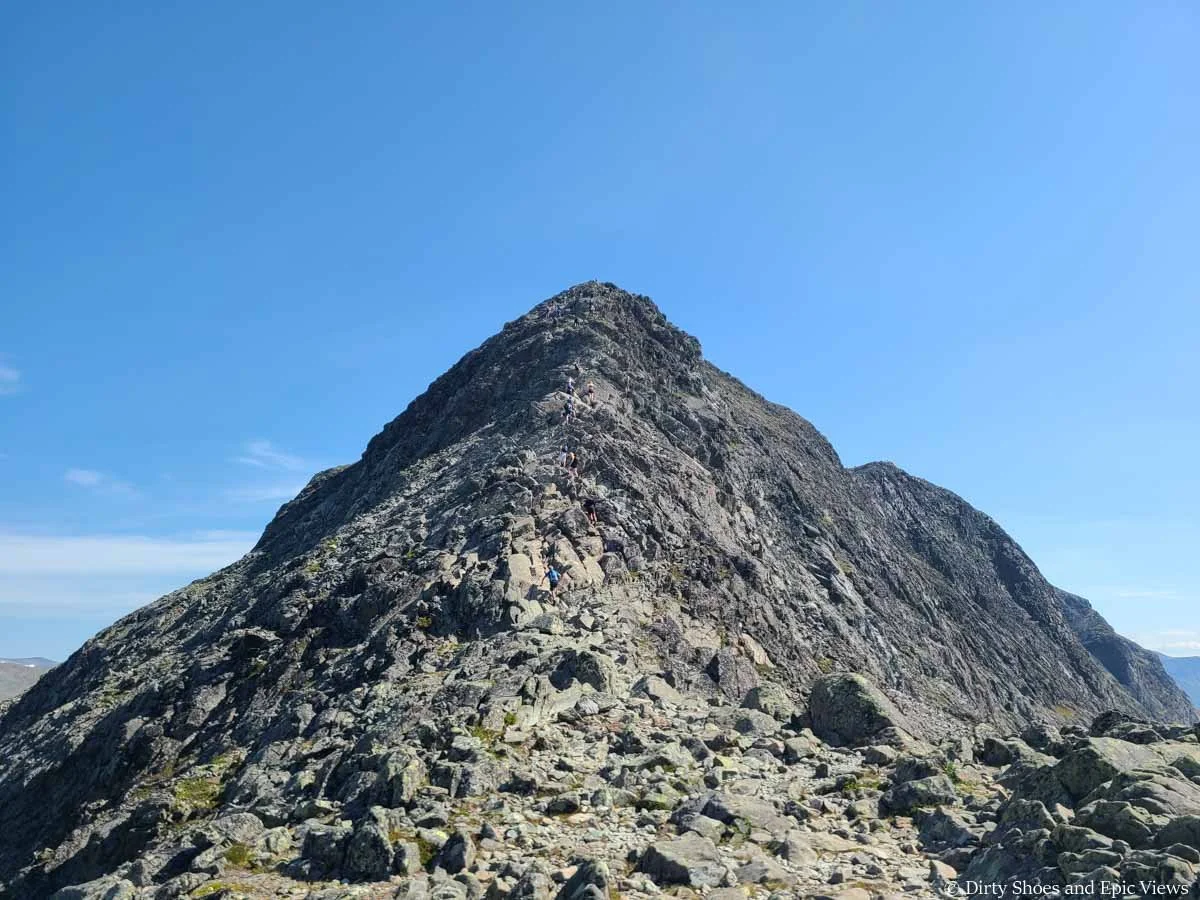 A line of hikers ascend a narrow rocky ridge along the Besseggen Ridge hike in Norway