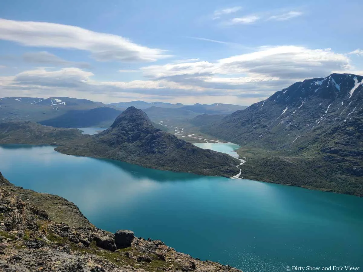 Small rocky mountains rise above a turquoise lake along the Besseggen Ridge trail in Norway