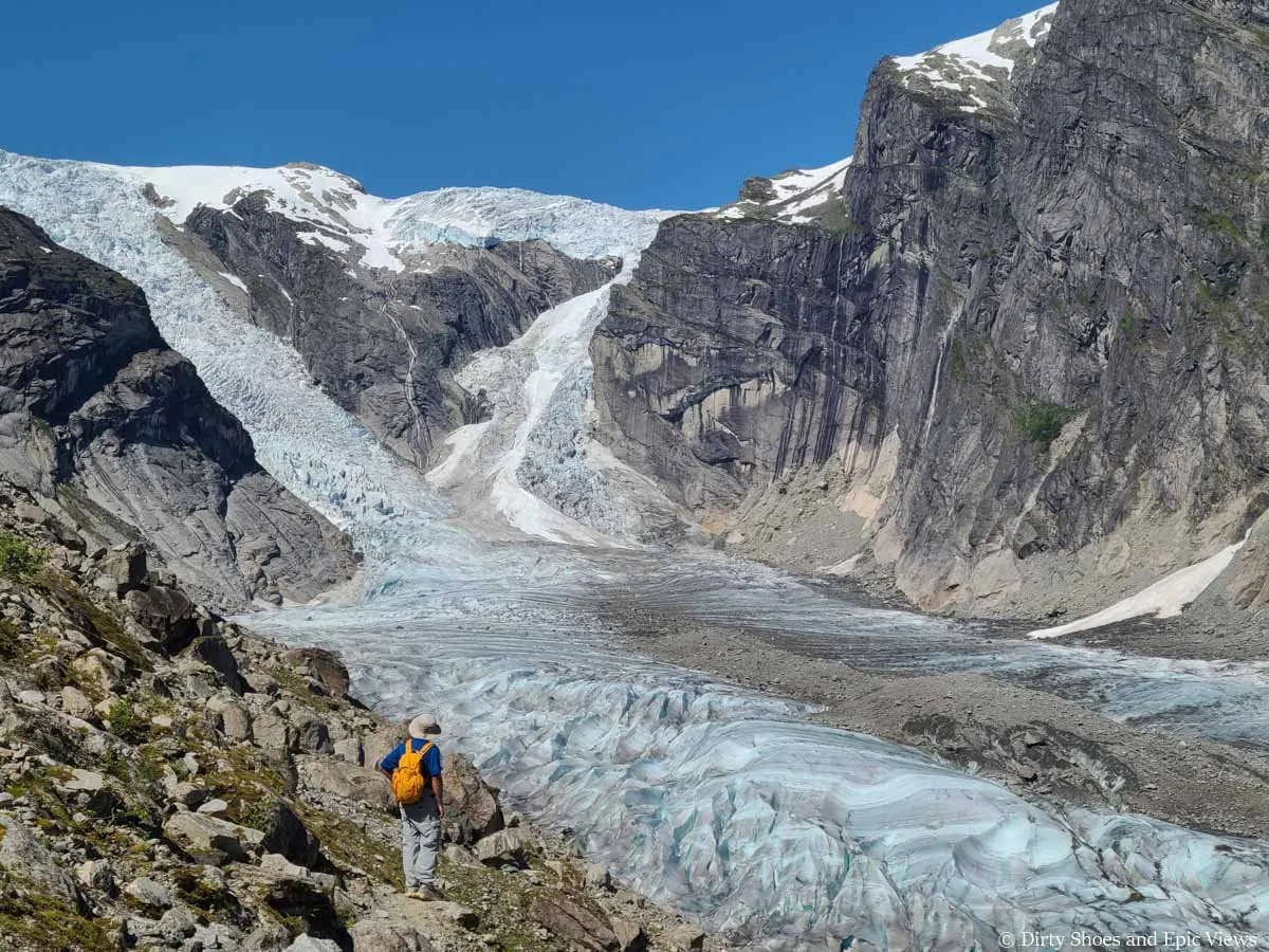 A hiker stands on a rocky slope overlooking an ice cap and glaciers at Austerdalsbreen in Norway