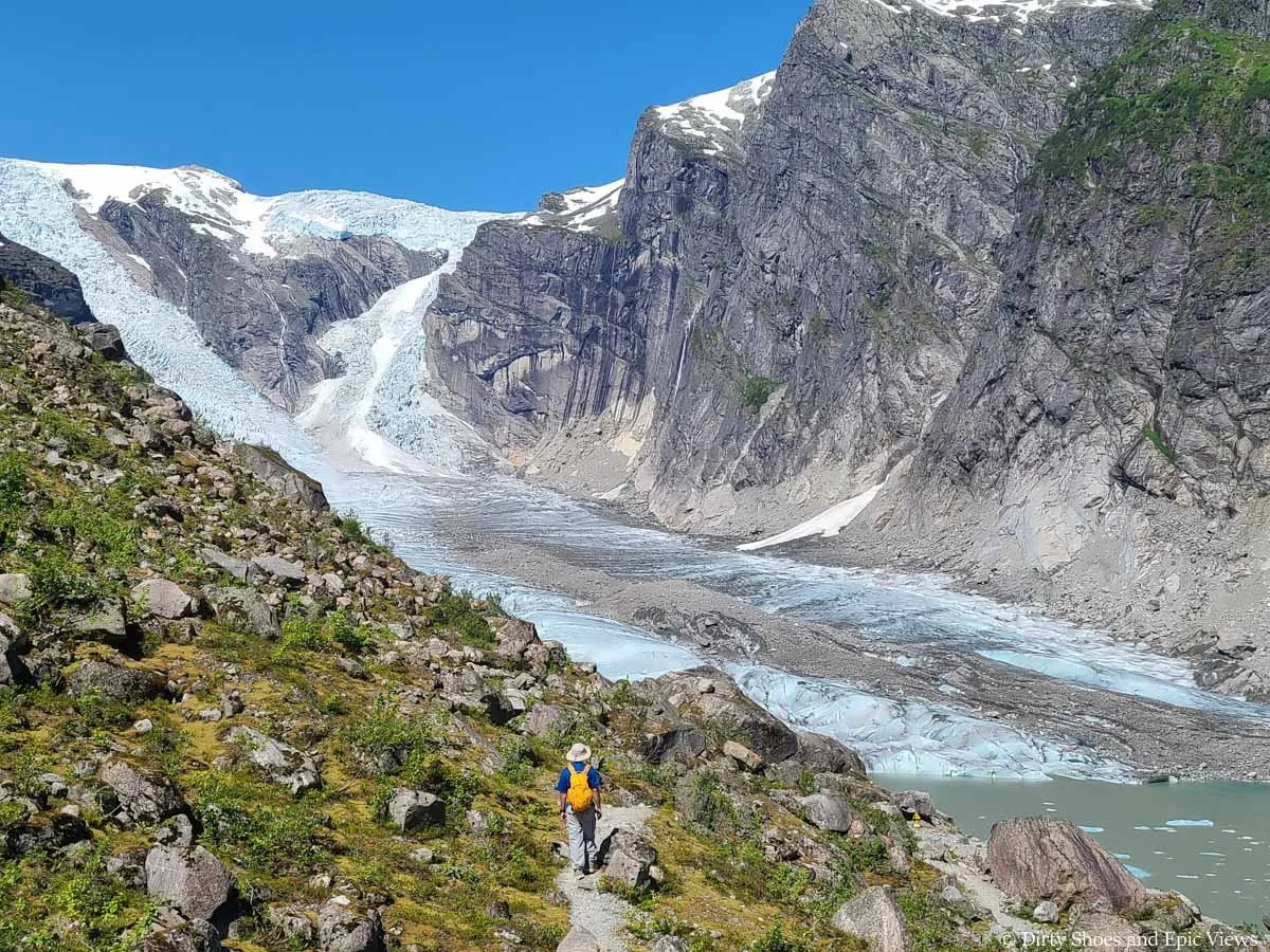 A hiker walks a rocky slope towards a view of a massive glacier at Austerdalsbreen in Norway