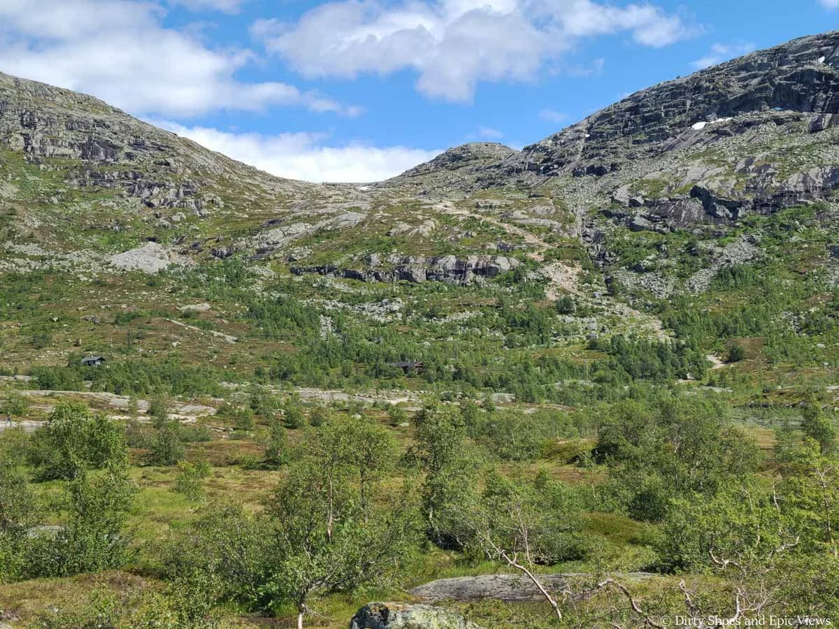 A mountain pass rises above a grassy meadow on the Trolltunga hike