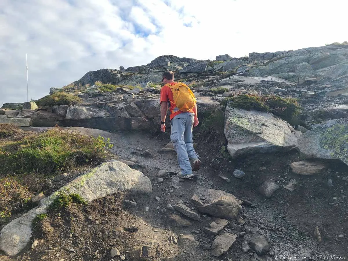 A hiker ascends a steep wet path through rocky terrain on the Trolltunga hike