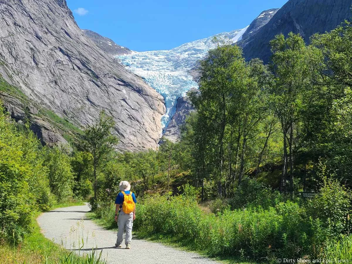 A hiker walks a paved path towards a glacier at Briksdalsbreen in Norway