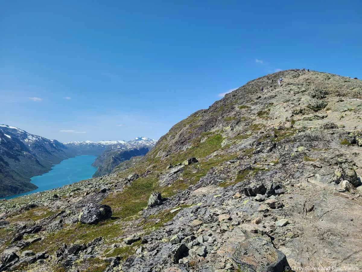 A rocky hill ascends above views of a blue lake on the Besseggen Ridge trail in Norway