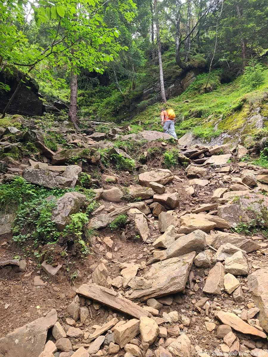 A hiker ascends a steep rocky path on the Reinanuten trail in Norway