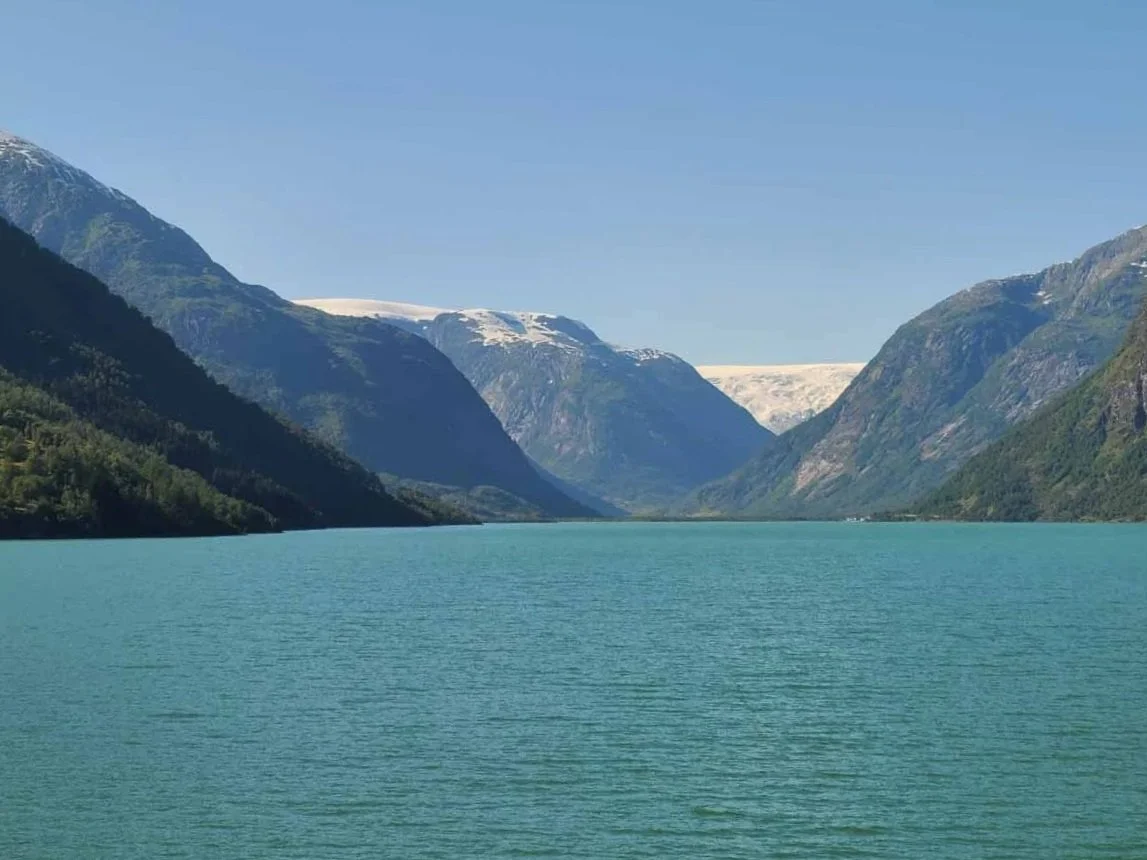 A view of a large blue lake backdropped by mountains and a glacier on the drive to Austerdalsbreen in Norway