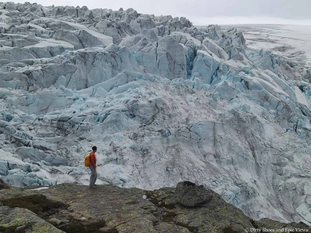 A hiker stands in front of a massive ice cap at the Reinanuten viewpoint in Norway