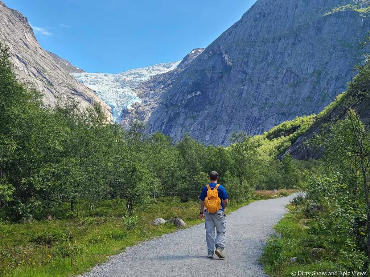 A hiker walks a flat gravel path towards a view of a glacier on the Briksdalsbreen hike in Norway