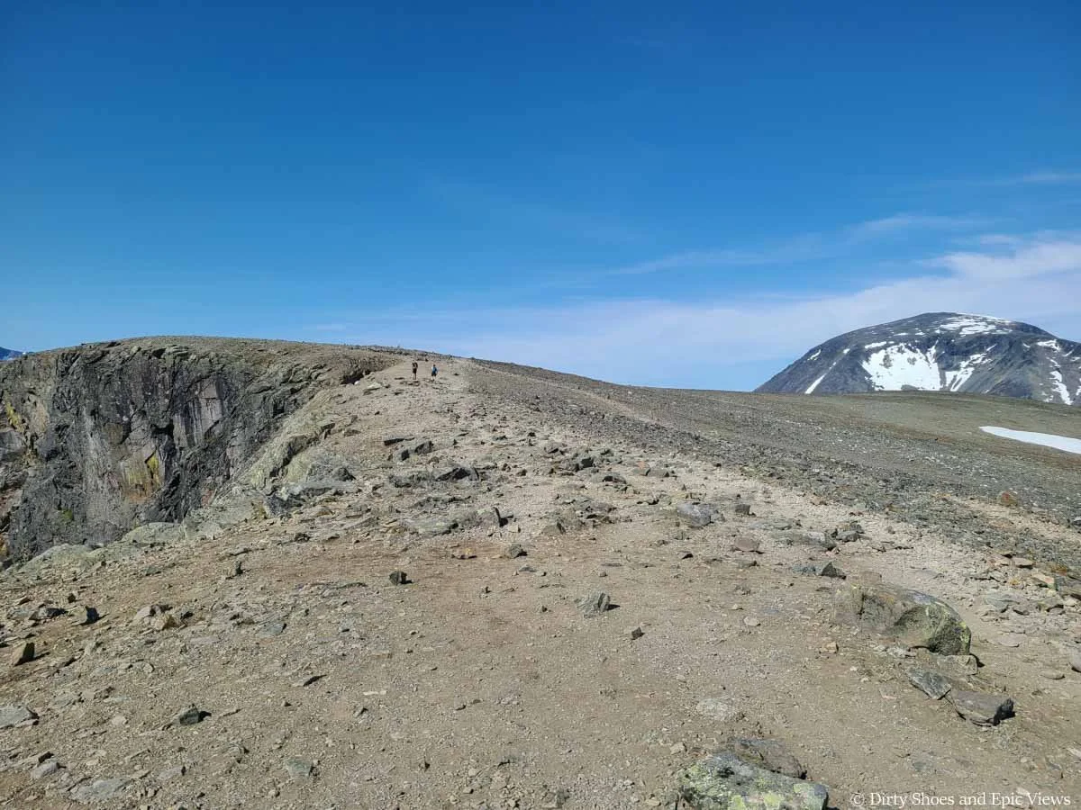 A pair of hikers walk along a trail near a cliff edge on the Besseggen Ridge hike in Norway