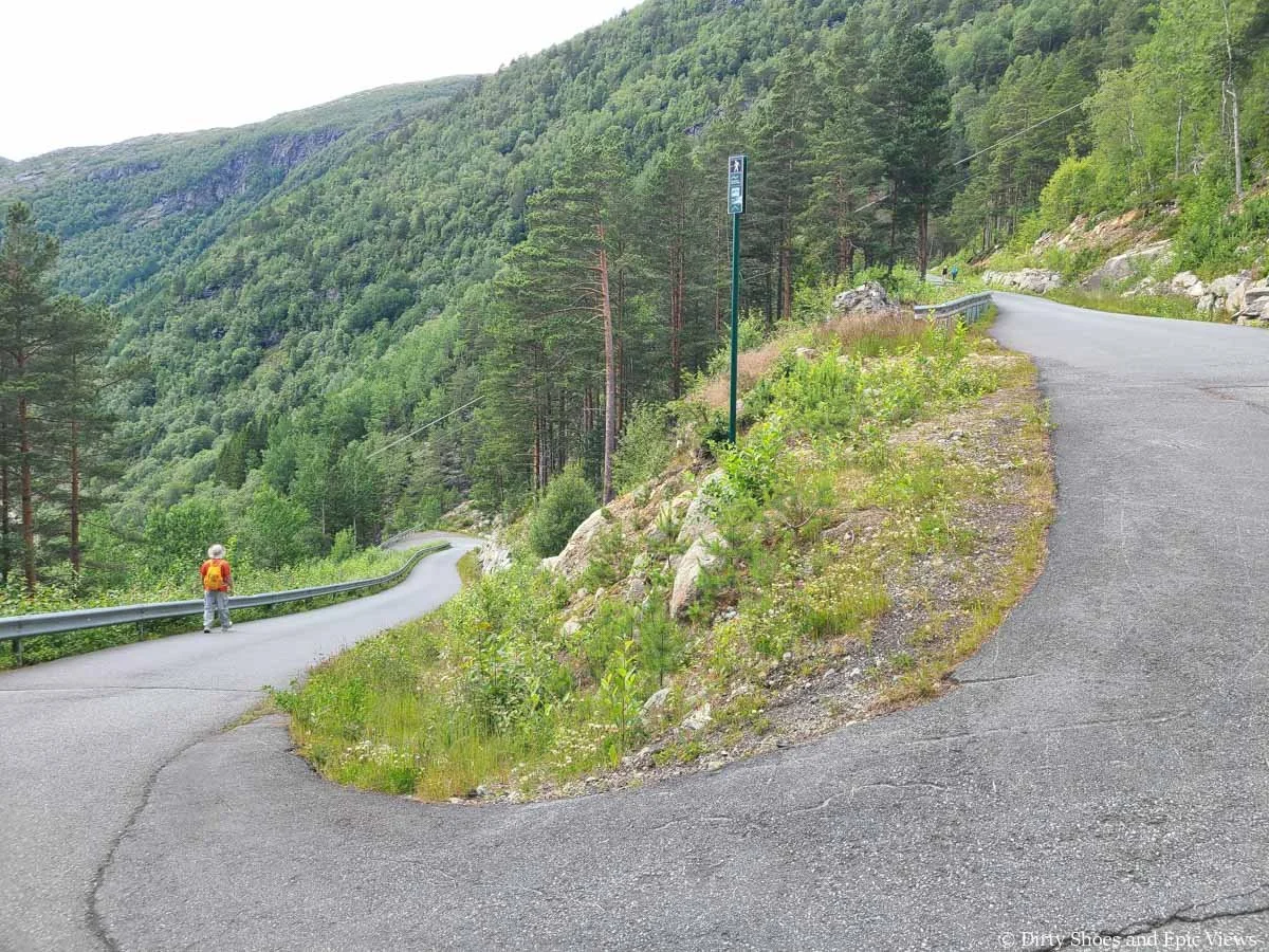 A narrow paved road steeply switchbacks up a mountainside between the P2 and P3 Trolltunga parking lots