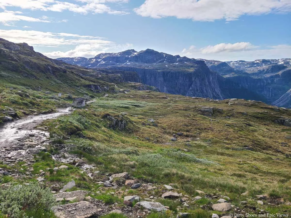 A narrow dirt path weaves its way through a grassy meadow towards mountain views on the Trolltunga hike