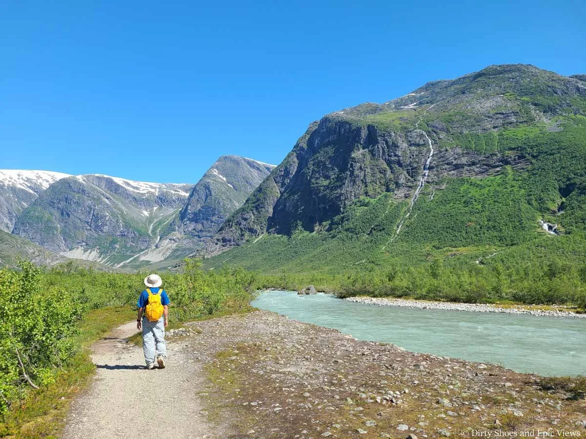 A hiker walks along a blue river surrounded by mountains on the Austerdalsbreen hike in Norway