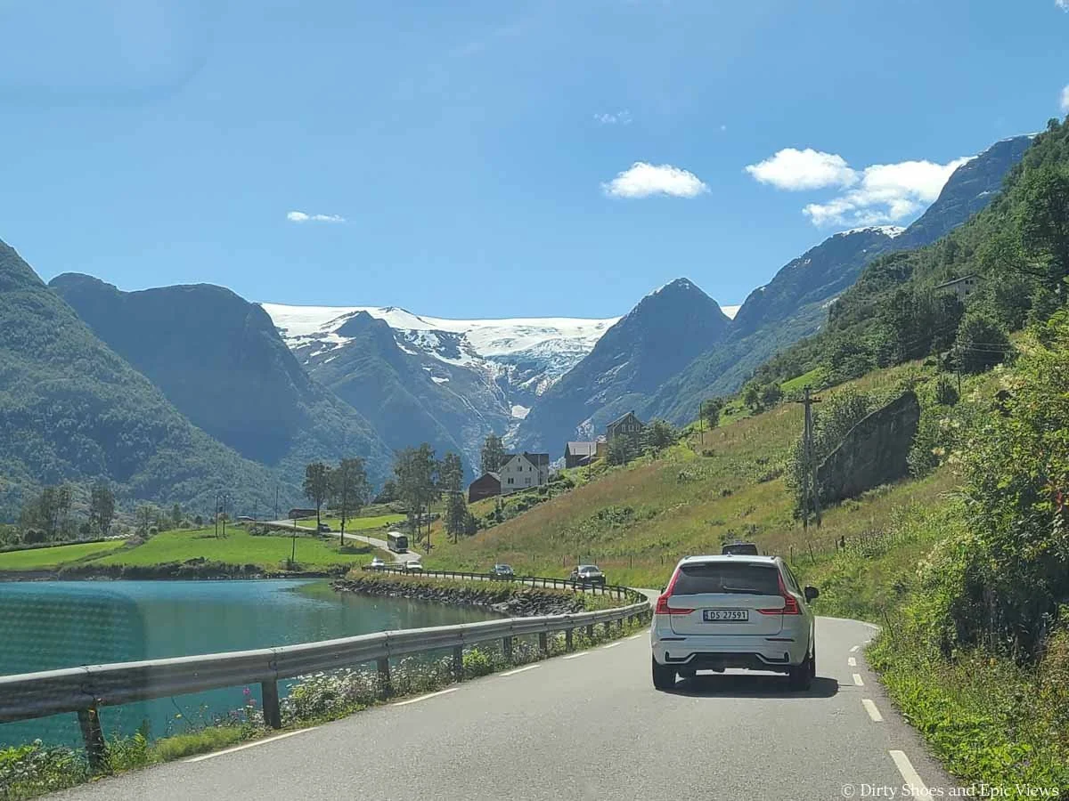 A car drives a narrow paved road towards countryside and mountain and glacier views on the road to Briksdalsbreen