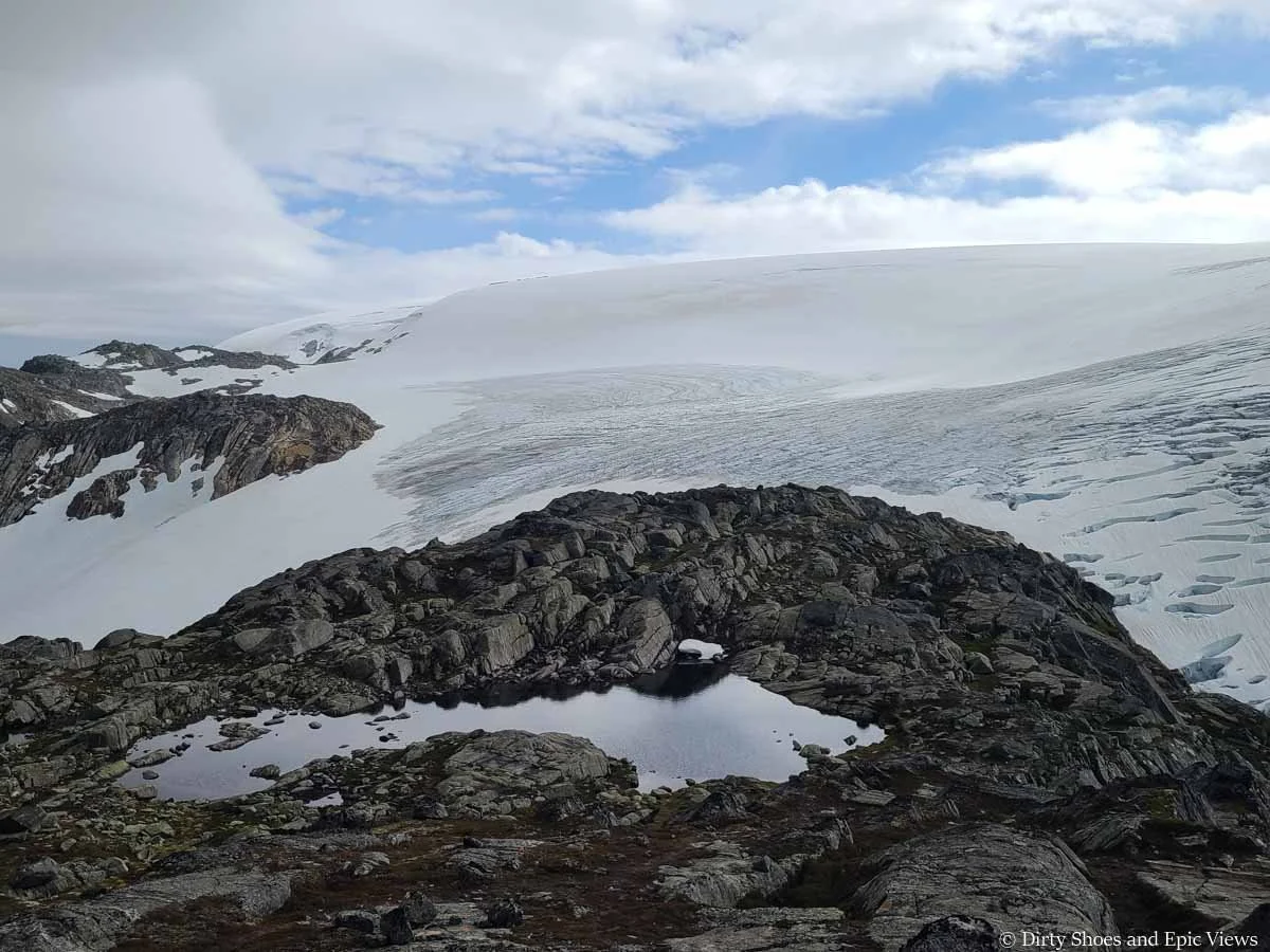 A small summit tarn sits on a rocky ridge in front of a massive ice cap at the Reinanuten viewpoint in Norway