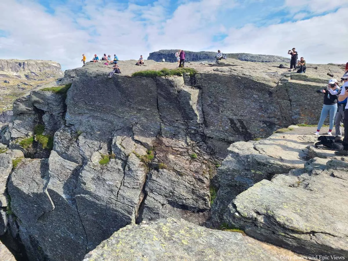 People stand on the edge of a steep cliff taking pictures near Trolltunga