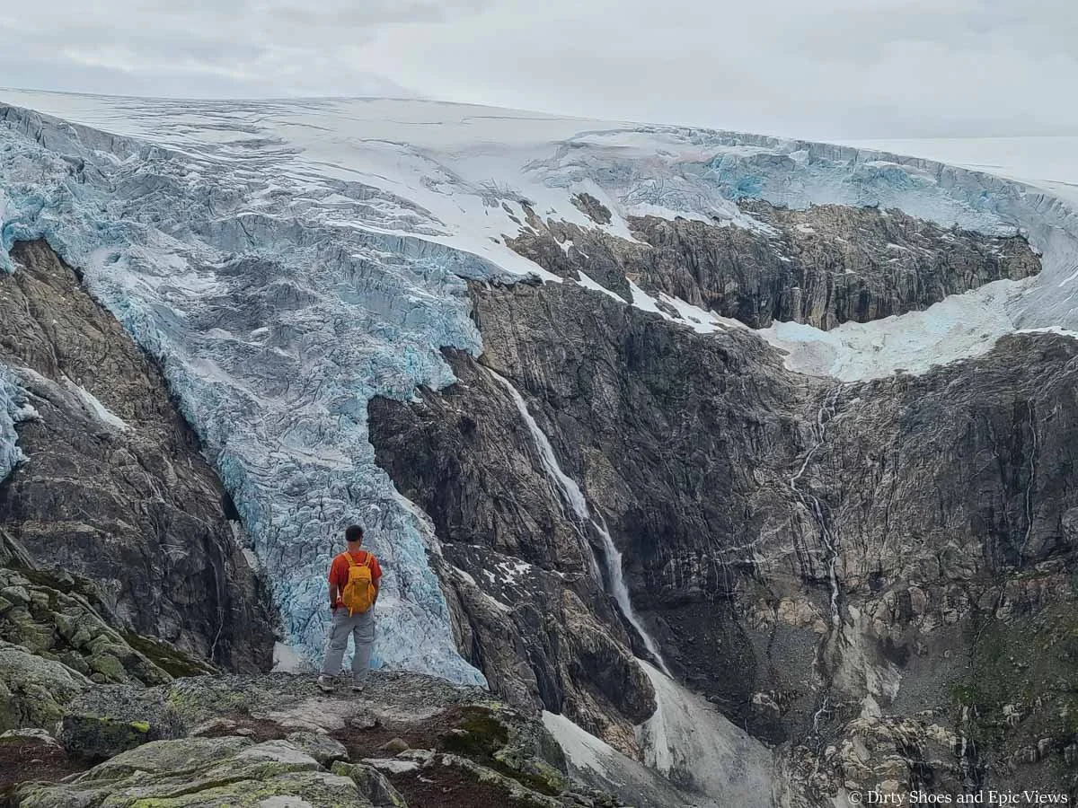 A hiker stands in front of views of a cascading glacier and waterfall on the Reinanuten hike in Norway