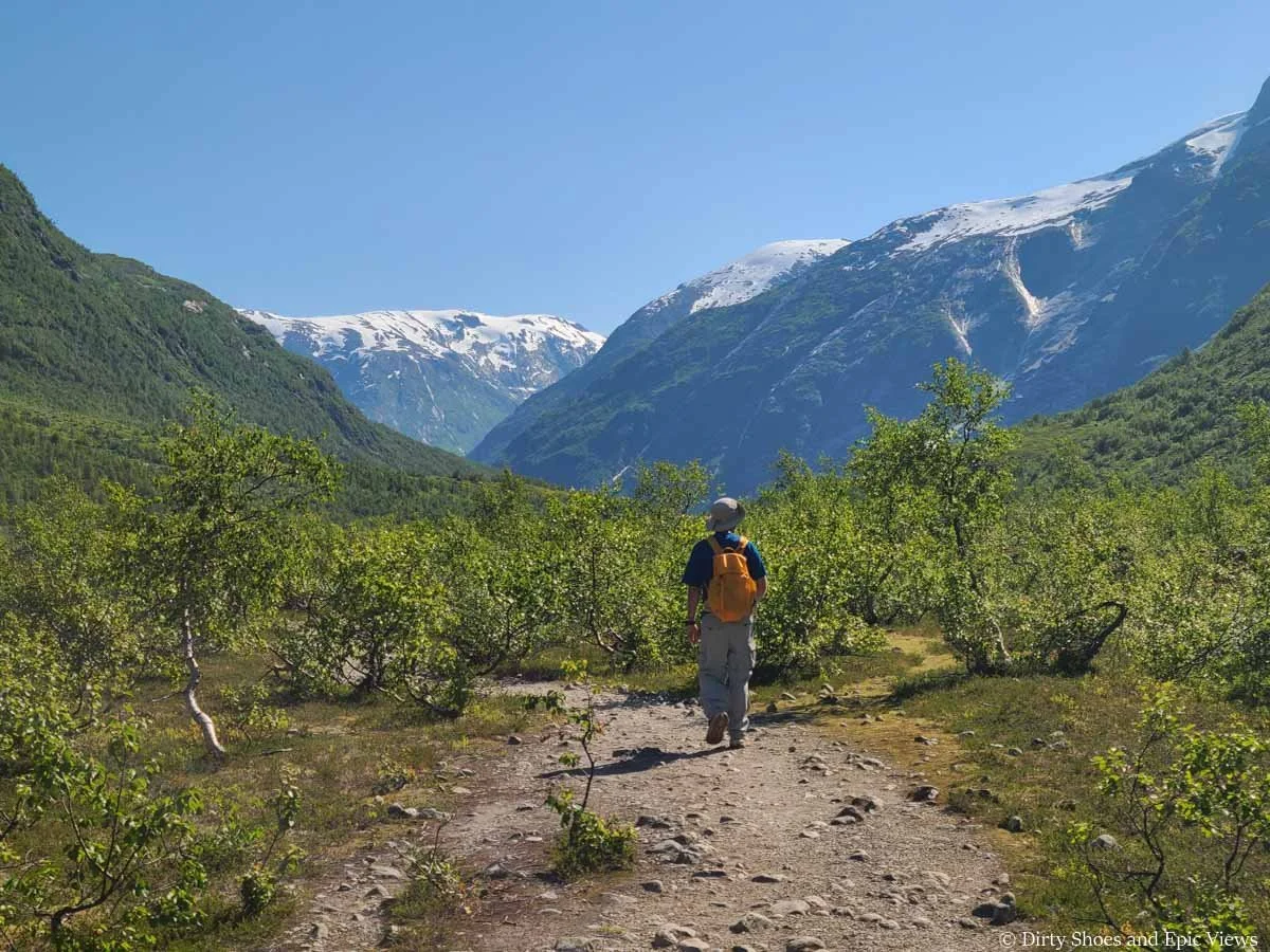 A hiker walks a wide dirt path towards mountain views on the Austerdalsbreen hike in Norway