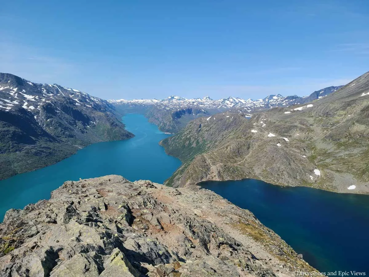 Snowy mountains backdrop a view of two blue lakes as seen from the Besseggen Ridge trail in Norway